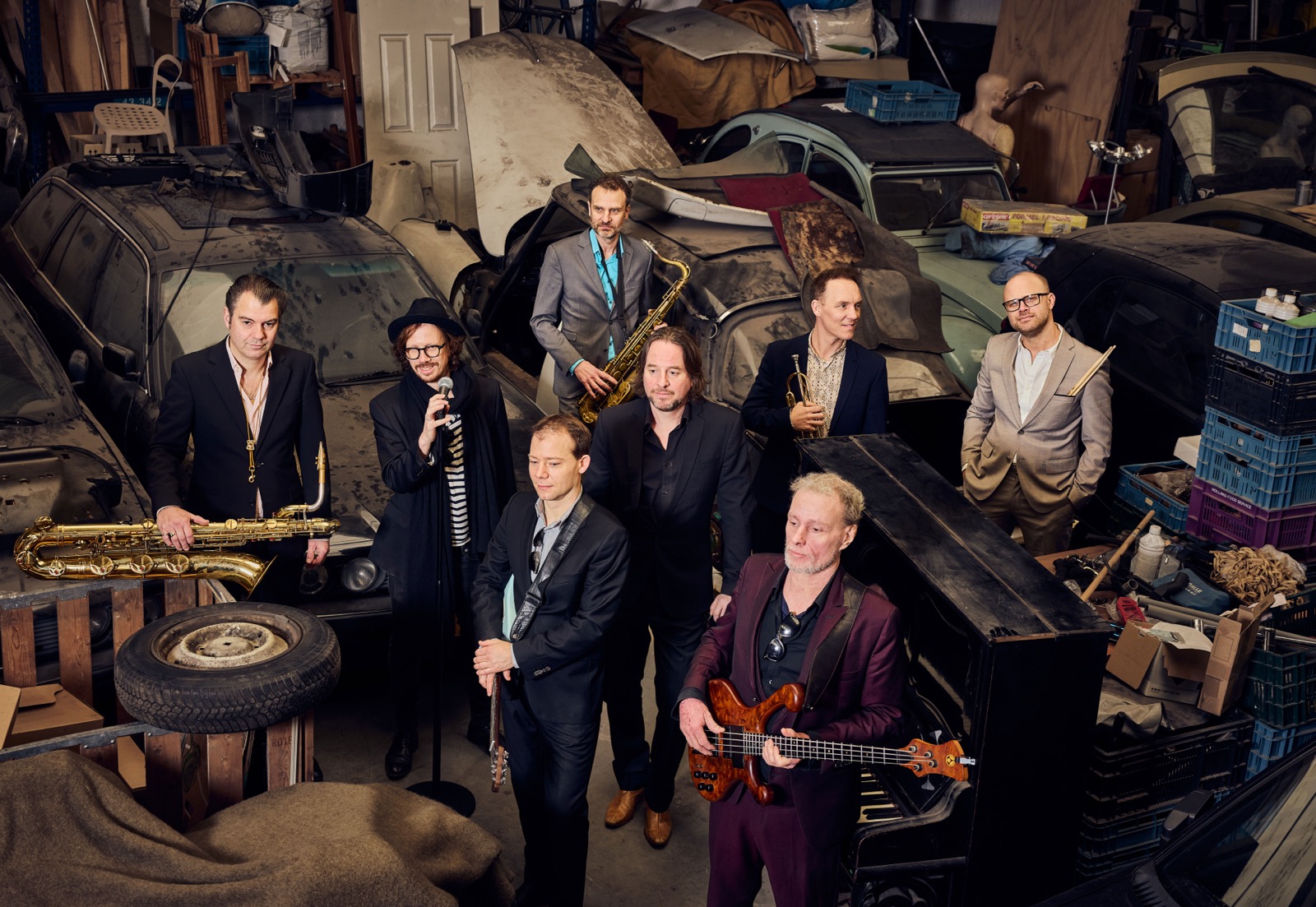 The Jig — eight members posed among vintage cars in a garage